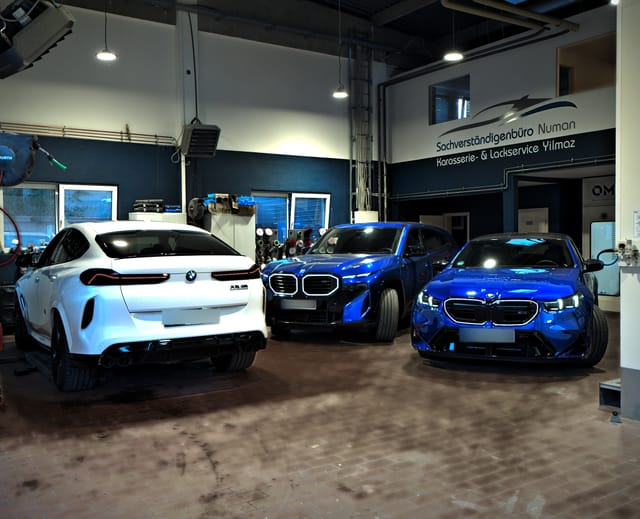 Blick durch die Halle mit einem weißen BMW X6 M und zwei blauen BMW