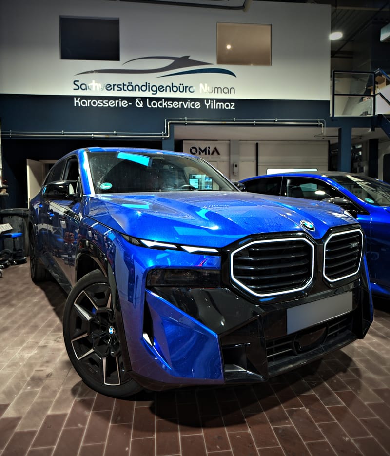 Blauer BMW XM in der Halle vor dem Firmenlogo an der Wand
