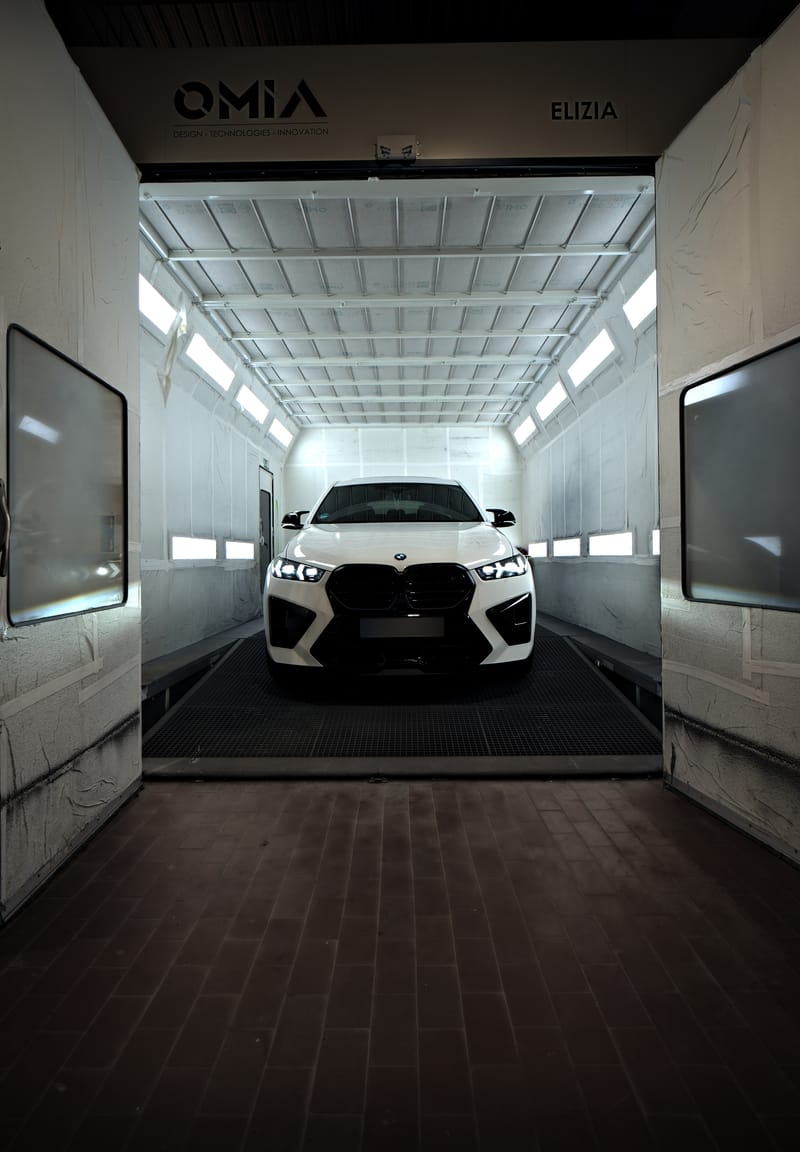 Blick durch das offene Tor in die Lackierkabine mit einem weißen BMW X6 M