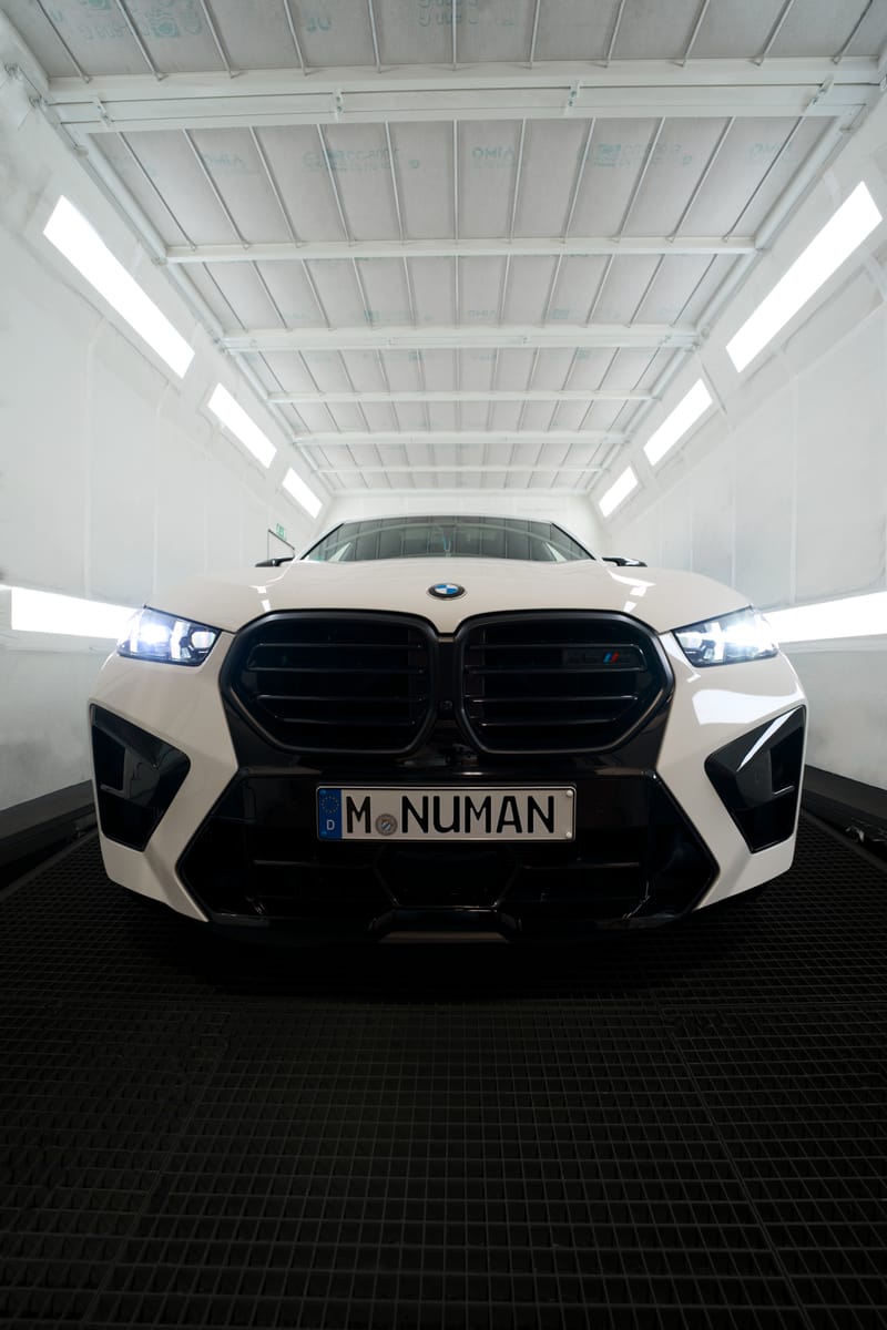 Weißer BMW X6 M mit eingeschalteten Scheinwerfern in der Lackierkabine